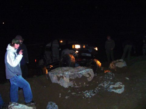 1993 Ford Bronco - An off-road vehicle is seen navigating a challenging rocky terrain in the dark, with its headlights illuminating the path.