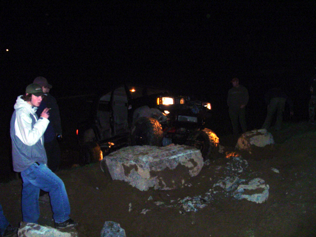 Off-road vehicle with headlights on, navigating rocky terrain at night