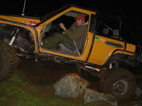 1993 Ford Bronco - This heavily modified yellow SUV is shown off-roading over rocks at night.