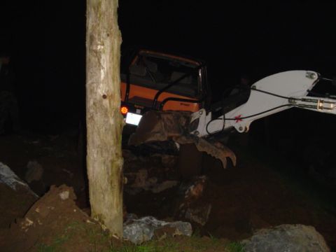 1993 Ford Bronco - An orange excavator with a claw attachment is seen operating at night, clearing debris.