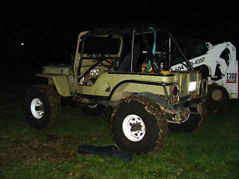 1993 Ford Bronco - A modified olive green Jeep CJ-5 sits on a grassy field next to a white skid steer loader at night.