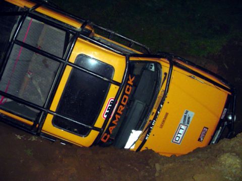 1993 Ford Bronco - This heavily modified off-road vehicle appears to be stuck in a muddy ditch, with visible aftermarket modifications and decals.