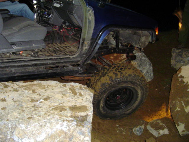 blue off-road vehicle with mud-caked tires navigating large rocks, interior visible