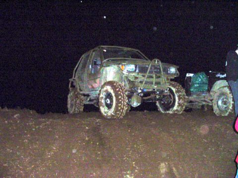 1993 Ford Bronco - Two heavily modified off-road vehicles are seen in a muddy area at night.