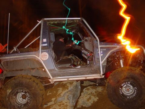 1993 Ford Bronco - Custom off-road vehicle with extensive roll cage modification seen during night driving.