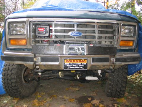 1986 Ford Bronco - A Ford truck's front end is visible, a winch and a humorous warning sticker.