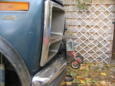 1986 Ford Bronco - Close-up of a blue vehicle's front end, showing the fender, bumper, and grille, with a small cart nearby.