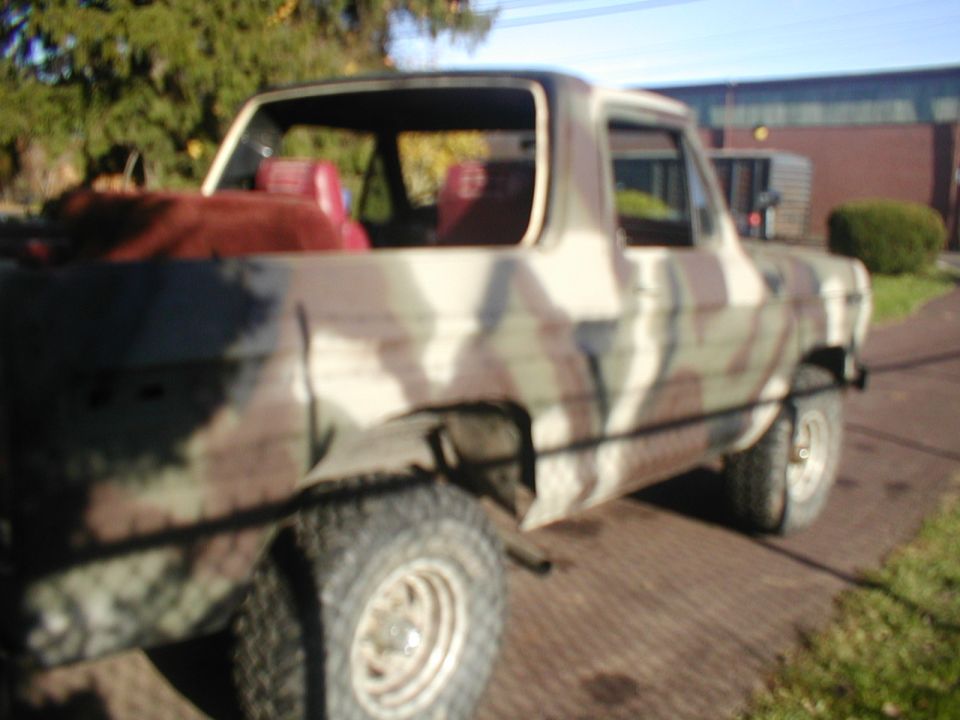 Desert-camo Ford Bronco with top removed, red seats and white steel wheels