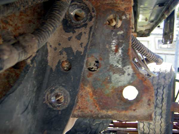 close-up of a heavily rusted metal bracket on a vehicle frame, with wires and a tire visible