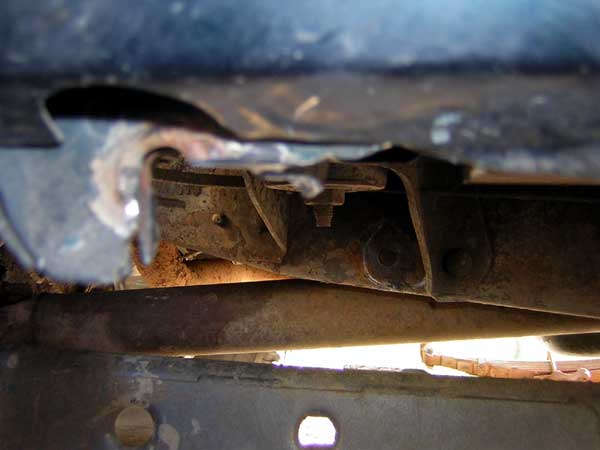 Rusty vehicle frame with visible bolts and suspension parts, close-up view