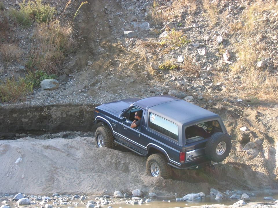 Blue Ford Bronco driving through a sandy, rocky ditch