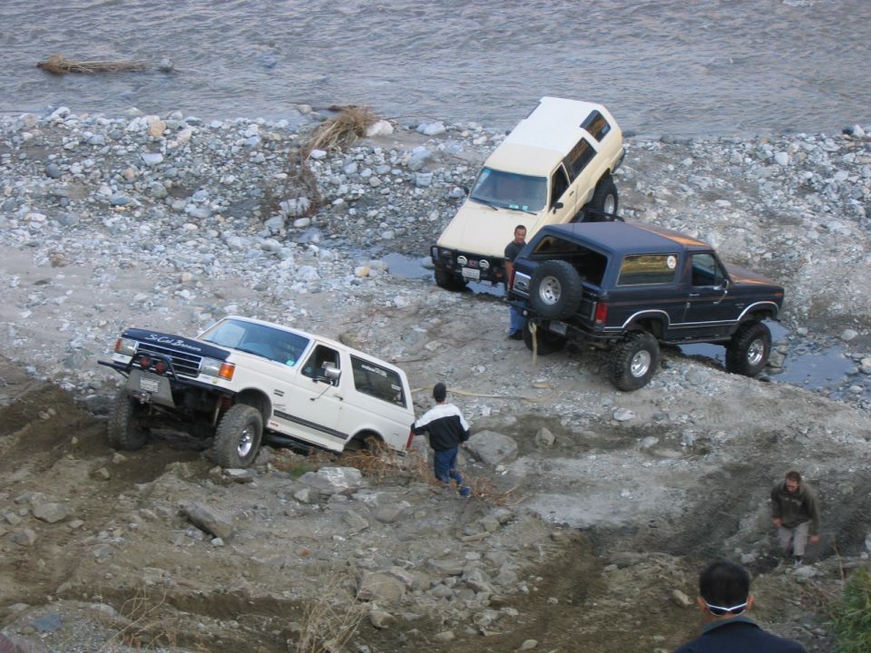 Three SUVs navigating a rocky riverbed, one white, one dark blue, and one tan