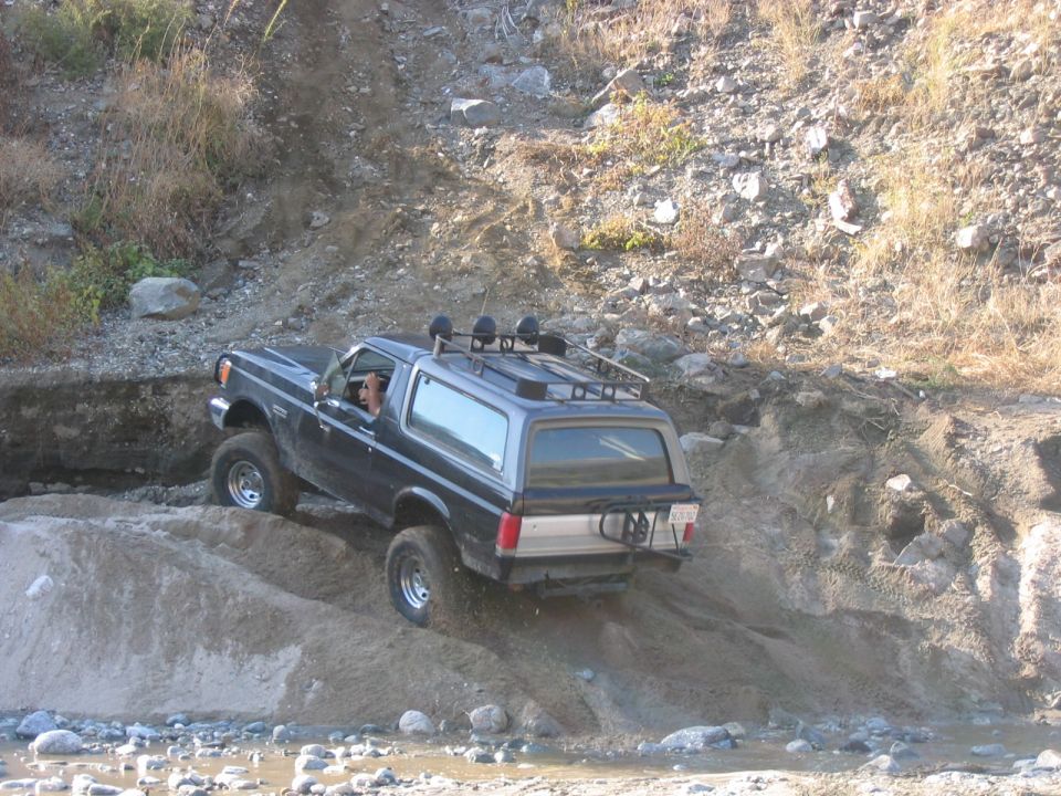 Ford Bronco climbing a dirt hill next to a rocky embankment
