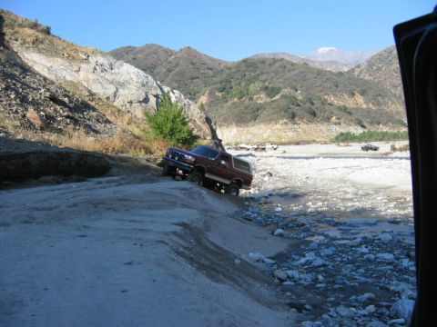 1985 Ford Bronco - A maroon Ford Bronco navigates a dry riverbed with mountainous terrain in the background.