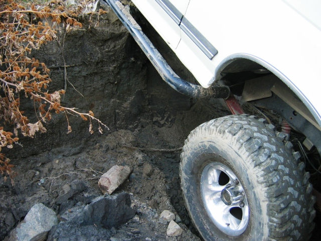 White SUV's muddy off-road tire and alloy wheel flexed over dirt and rocks