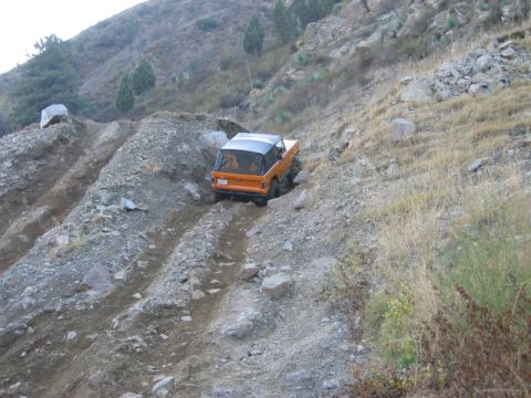 1985 Ford Bronco - An orange SUV navigates a challenging, rocky incline on a dry, mountainous terrain.