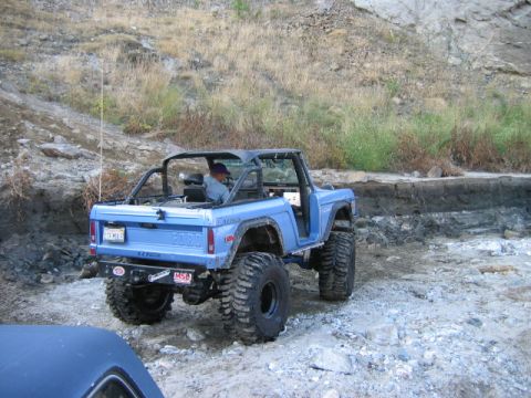 1985 Ford Bronco - A lifted blue Ford Bronco is driven off-road on a rocky, dirt trail.