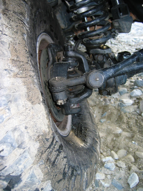 1985 Ford Bronco - The suspension and tire of an off-road vehicle are shown in a close-up view on a rocky terrain.