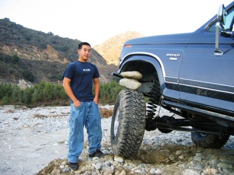 1985 Ford Bronco - A blue 1985 Ford Bronco is shown with a person standing next to its lifted suspension and large off-road tires.