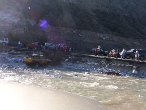 2000 Ford F-450 - A group of vehicles and people are gathered near a river, with some vehicles navigating the water.