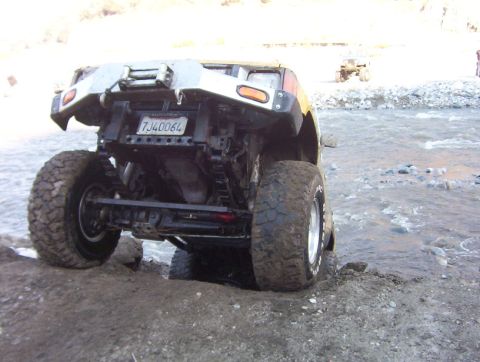 2000 Ford F-450 - An off-road vehicle navigates a rocky, watery terrain, showing its rear end and large tires.
