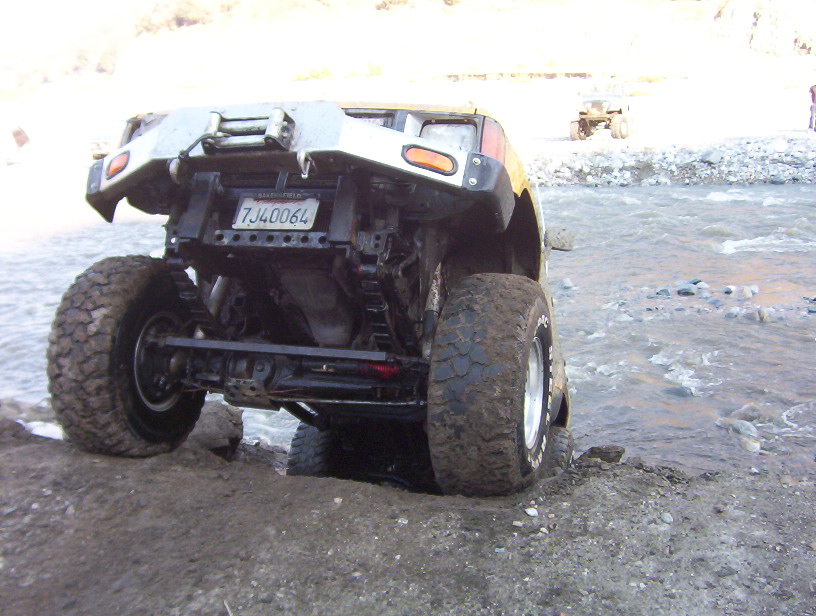 Off-road vehicle with large tires stuck in mud near water, rear view