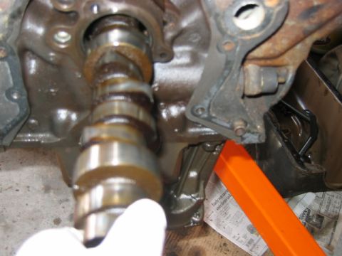1992 Ford Bronco - Close-up of a camshaft being installed or removed from an engine block or cylinder head, with visible lobes and journals. A gloved hand sup…