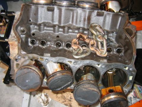 1992 Ford Bronco - A disassembled V-configuration engine block sits upside down on a workbench, showing four pistons at various heights within the cylinder bo…