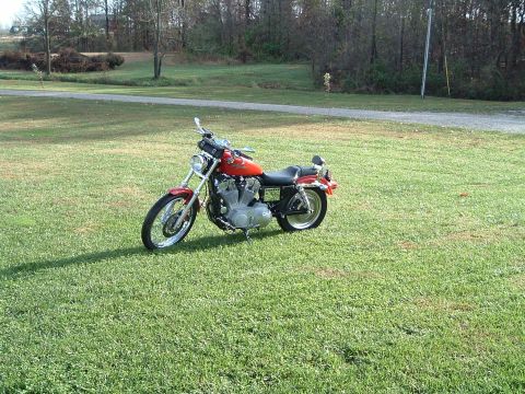 1995 Mercury Grand Marquis - Orange Harley-Davidson motorcycle parked on a grassy field with trees in the background.