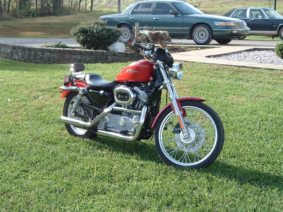 Red motorcycle parked on grass, with a green sedan in the background