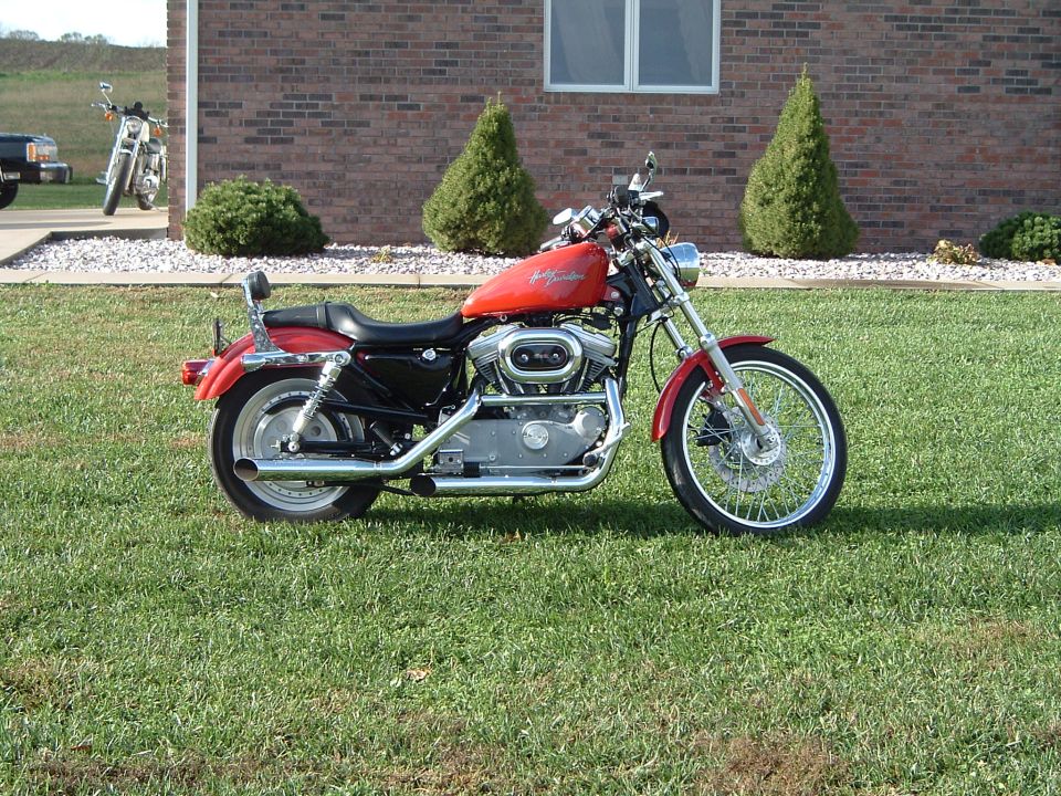 Red Harley-Davidson motorcycle parked on grass, another motorcycle in background