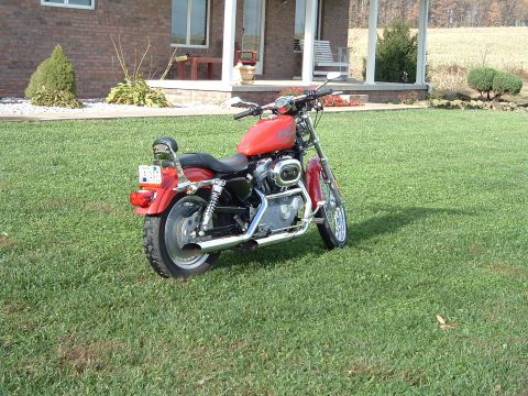 1995 Mercury Grand Marquis - A red motorcycle is parked on a grassy lawn in front of a brick house with a porch.