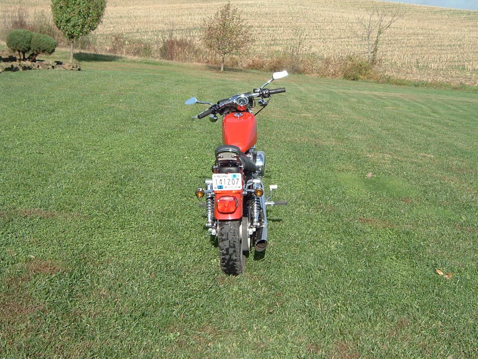 Red motorcycle rear view, parked on grass with a field in the background
