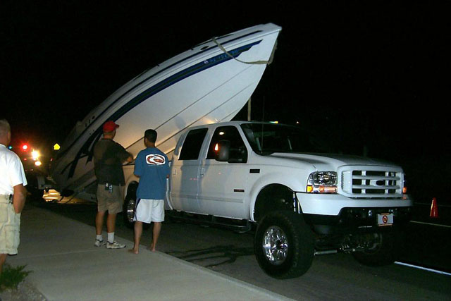 White lifted Ford Super Duty truck towing a boat trailer at night