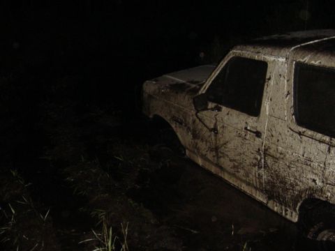 1989 Ford Bronco - A heavily mud-splattered 1987 Ford Bronco is partially submerged in dark, wet ground.