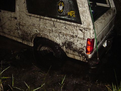 1989 Ford Bronco - This white SUV, heavily caked in mud, appears to be stuck in a dark, wet environment.