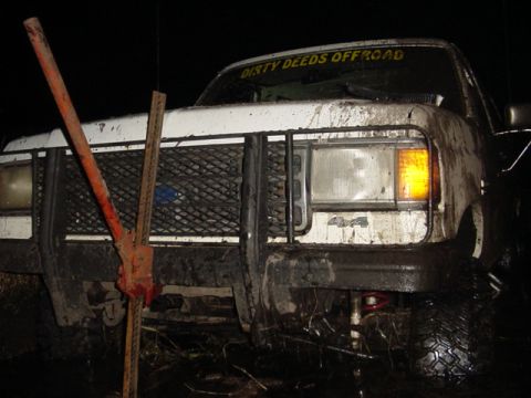 1989 Ford Bronco - A white Ford Bronco is stuck in the mud, with a jack positioned on its front grille.