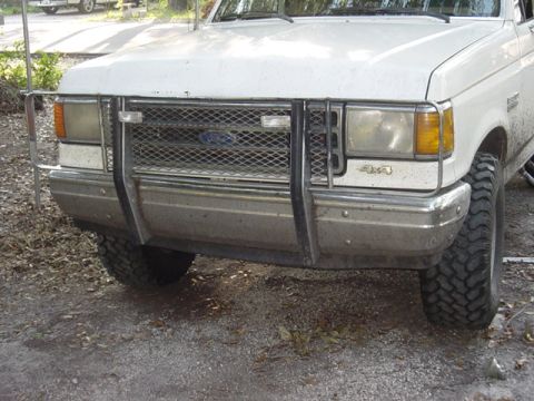 1989 Ford Bronco - The front grille and bumper of a white Ford truck are visible, a brush guard and a 4x4 emblem.