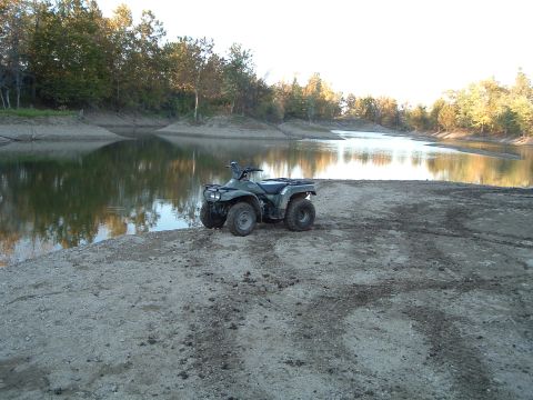 1995 Mercury Grand Marquis - An all-terrain vehicle sits on a muddy shore beside a calm lake with trees in the background.