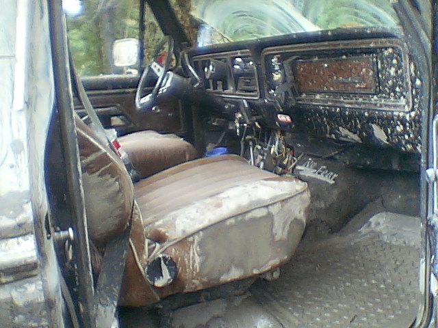 Rough interior of a Ford Bronco with torn brown bench seats, exposed dash wiring, and mud-splattered dashboard