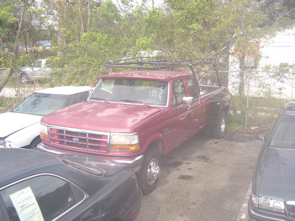 Red Ford F-Series truck with a ladder rack parked next to other vehicles