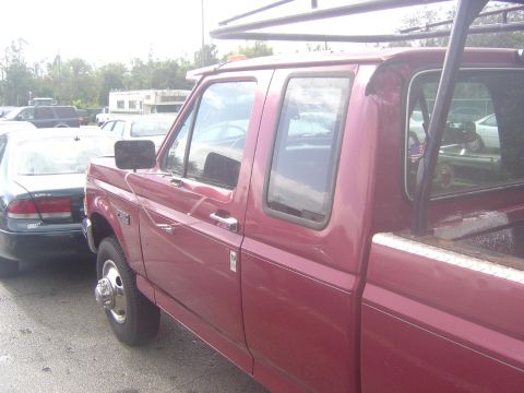 1993 Ford Bronco - A red pickup truck is parked next to a dark sedan in a lot.