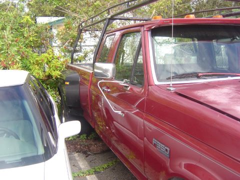 1993 Ford Bronco - This red Ford F-350 pickup truck is parked next to a white car, showing its side profile.