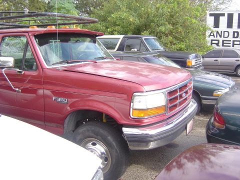1993 Ford Bronco - A red Ford F-350 truck is parked next to other vehicles, with a "Tires and Detail" sign in the background.