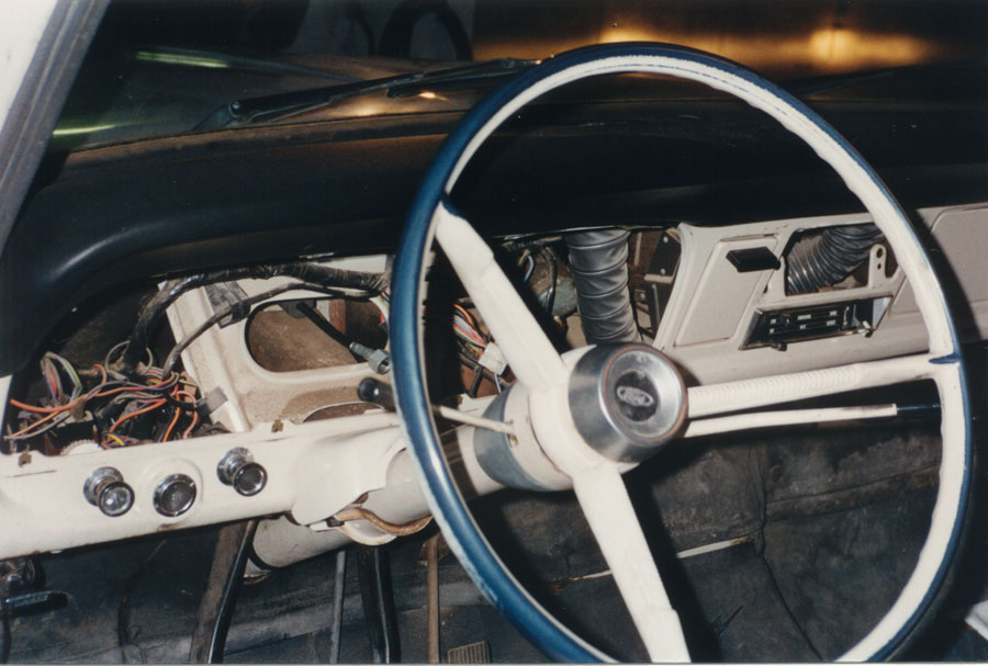 Classic Ford pickup dash with gauge cluster removed, wiring exposed, blue-rim steering wheel