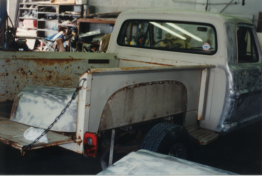Weathered classic pickup rear three-quarter with tailgate down and stripped rusty bed sides
