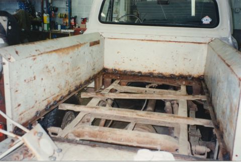 1968 Ford F-100 - Looking down into the bed of a classic pickup with the wood floor and cross planks removed, exposing the rusty frame rails, crossmembers, d…