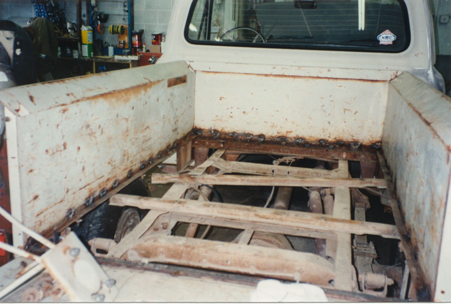 Pickup bed with floor removed showing rusty frame rails, driveshaft and bed bolt holes