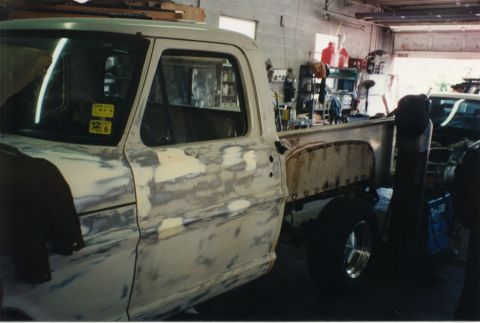 1968 Ford F-100 - Left front three-quarter view of a classic Ford pickup in a body shop with bodywork in progress, the door and cab show sanded-through paint…