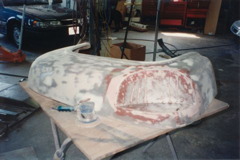 1968 Ford F-100 - A removed truck front fender sits upside down on a plywood-topped work table in a body shop, block-sanded through primer with pink filler a…